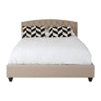 Beige king bed with a tufted headboard, featuring a white mattress and decorative black and white chevron-patterned pillows. The bed is supported by dark wooden legs