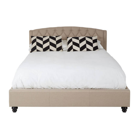 Beige king bed with a tufted headboard, featuring a white mattress and decorative black and white chevron-patterned pillows. The bed is supported by dark wooden legs