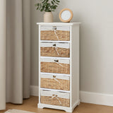 A tall, white wooden chest with five woven seagrass drawers, featuring a simple design and a small round clock and a potted plant on top, set against a light-colored wall and wooden floor