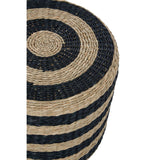 Round pouffe made from seagrass, featuring alternating black and natural tan stripes. The texture is woven, showcasing a circular pattern with a smooth top surface