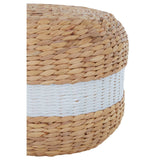 Round pouffe made from natural water hyacinth with a textured surface, featuring a prominent white stripe around its midsection. The pouffe has a warm, earthy tone and a woven design that adds a rustic touch to home decor