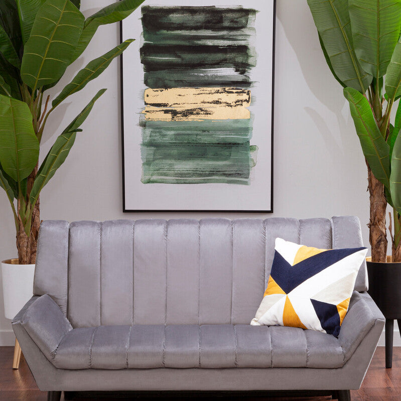 A grey two-seat sofa with a tufted design, positioned in a modern living space. The sofa features black legs and is adorned with a colorful geometric throw pillow. Behind the sofa, there is a large framed abstract artwork and two tall green plants, creating a stylish and inviting atmosphere. The floor is made of warm wood, adding to the cozy ambiance