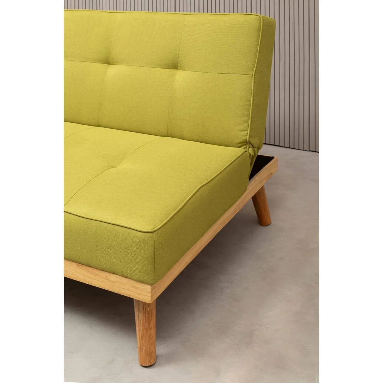 Green fabric sofa with tufted seat, wooden frame, and angled legs on light floor