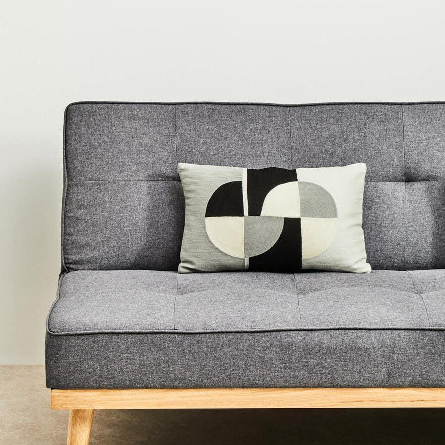 Grey fabric sofa with wooden legs and a geometric black and cream cushion on seat