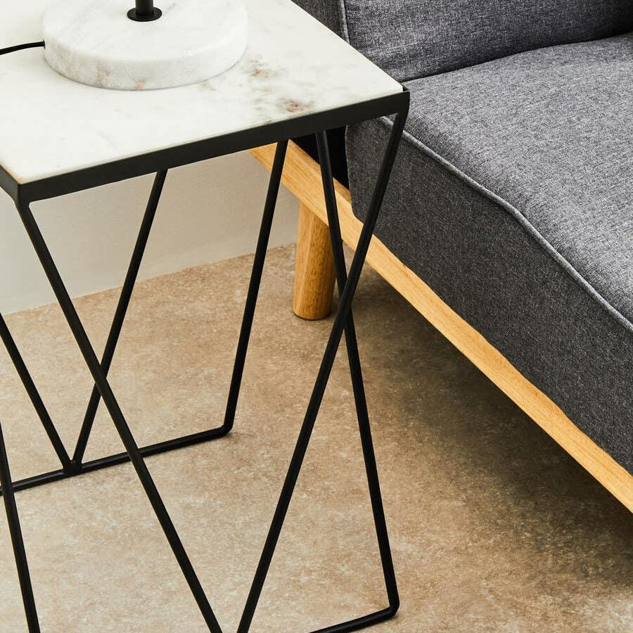Marble top side table with black metal frame beside grey fabric sofa on wooden legs
