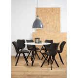 Round dining table with a marble effect top surrounded by six black upholstered chairs, set against a light-colored wall and a textured wooden backdrop. A large gray pendant light hangs above the table, which is styled with a small decorative centerpiece. The floor is wooden, adding warmth to the modern aesthetic