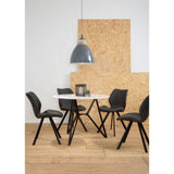 Round dining table with a marble effect top surrounded by six black chairs, set against a light-colored wall and a textured wooden backdrop. A modern pendant light hangs above the table, creating a stylish dining area