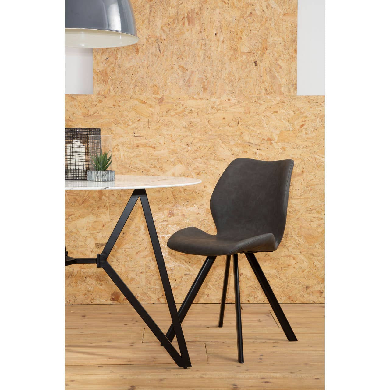 Round dining table with a marble effect top, accompanied by six stylish chairs featuring a dark fabric seat and black metal legs. The setting includes a light-colored wooden floor and a textured wall in the background, creating a modern and inviting atmosphere