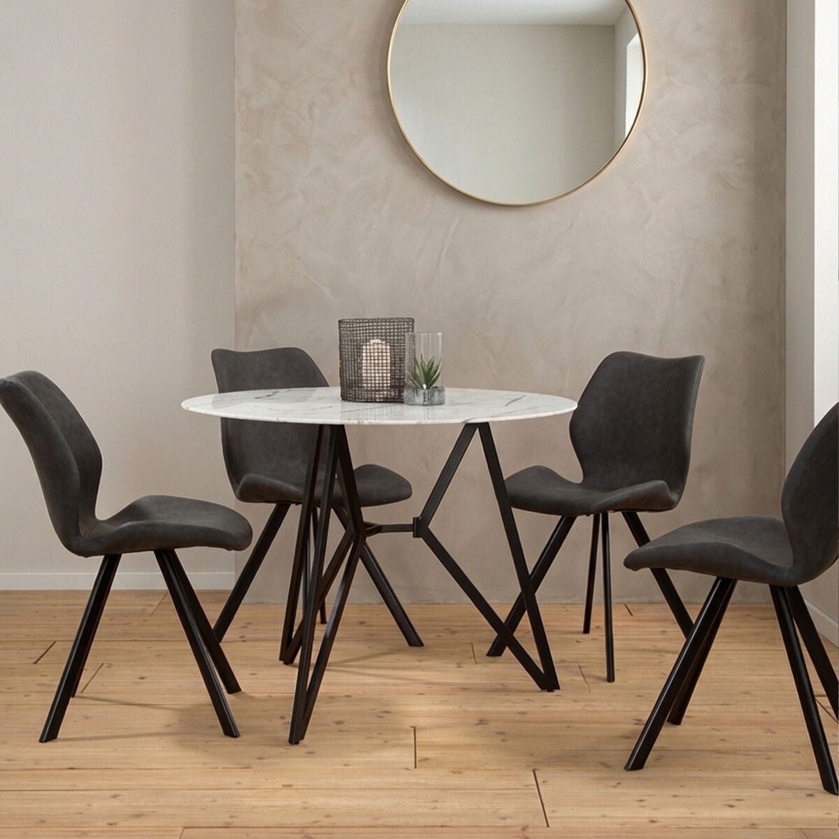 Round dining table with a marble effect top, surrounded by six modern black chairs with angled legs. The setting features a light-colored wall and a round mirror in the background, with a decorative centerpiece on the table. The floor is made of light wood