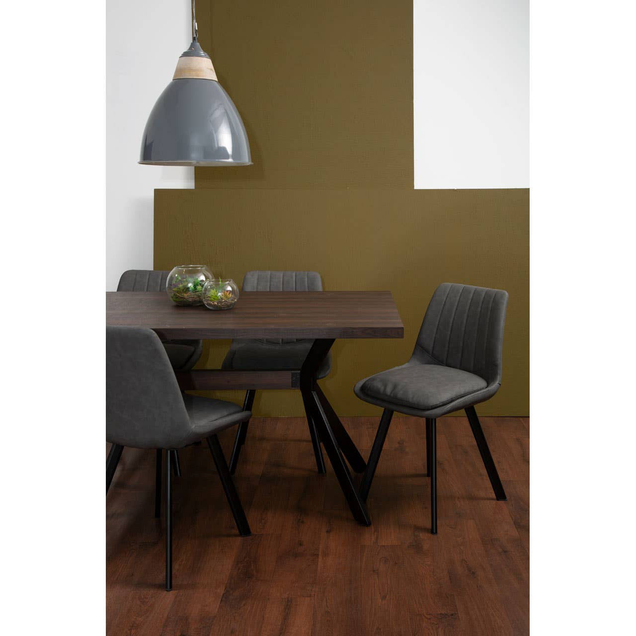Westford rectangle dining table with a dark wood finish, accompanied by six modern gray chairs. The table features a unique angled base, and the setting includes a stylish pendant light overhead, with a green accent wall in the background and a wooden floor. A small decorative bowl sits on the table