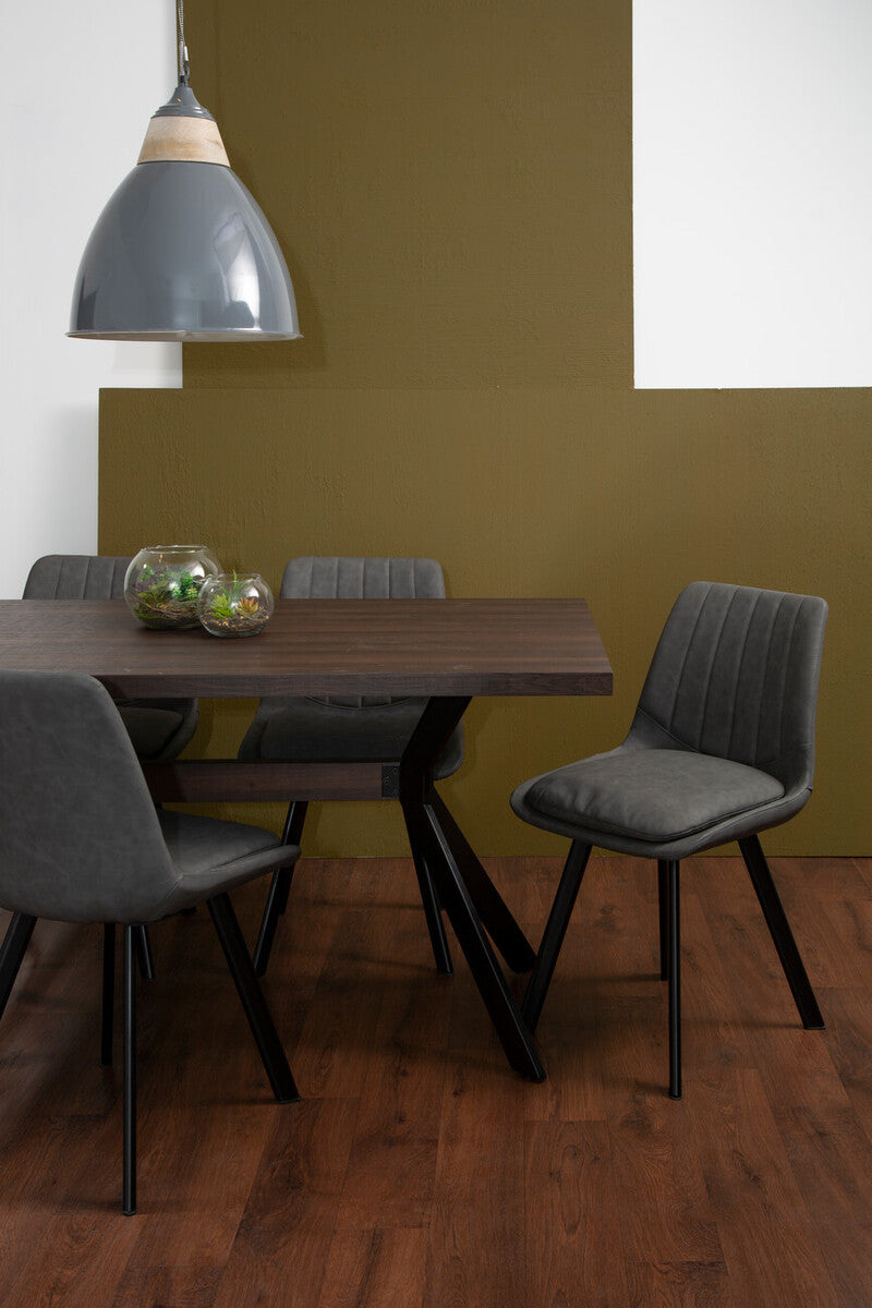 Rectangle dining table with a dark wood finish and six matching chairs featuring gray upholstery. The table has a modern design with angular black legs, and the chairs have a sleek, minimalist look. A pendant light hangs above the table, and the background features a muted olive green wall and a white wall, with a wooden floor visible. A small decorative bowl sits on the table