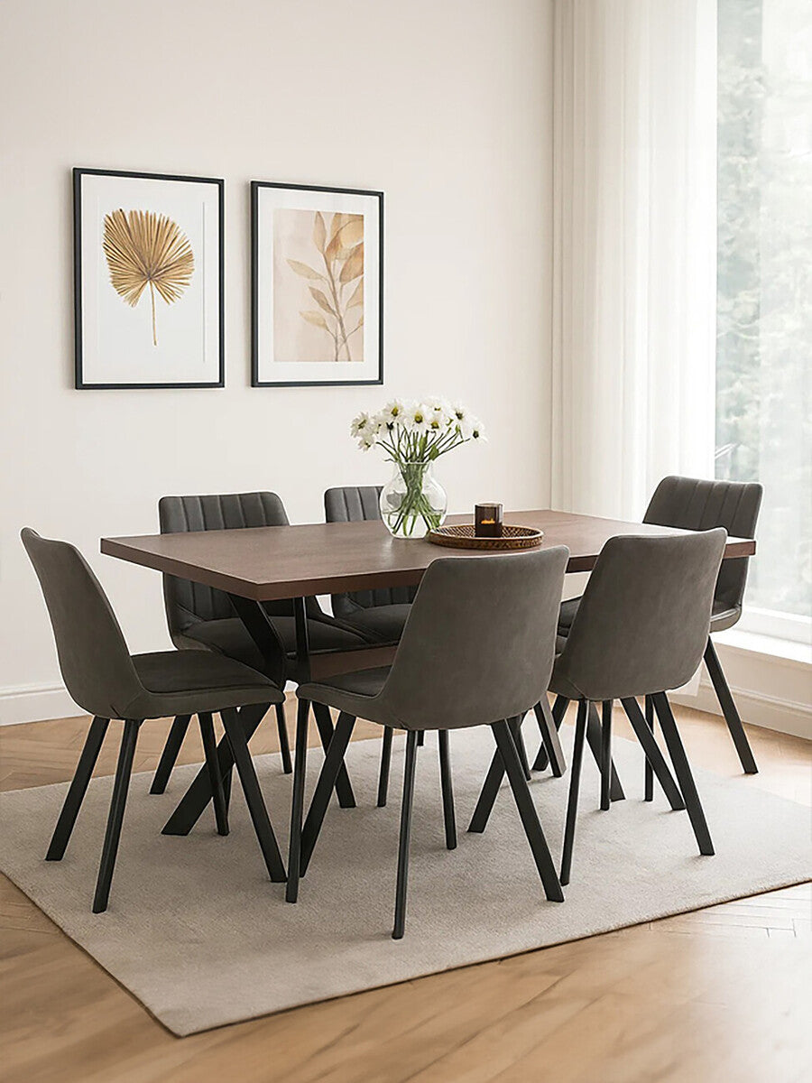 Rectangle dining table surrounded by six modern chairs, set on a light-colored rug. The table features a wooden surface with a rich finish, while the chairs have a sleek design with dark upholstery. Two framed artworks hang on the wall in the background, and a vase with flowers sits on the table, creating a warm and inviting dining space. Natural light streams in from a nearby window, enhancing the overall ambiance