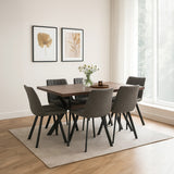 A rectangular wooden dining table surrounded by six upholstered chairs with dark legs, set in a bright room with large windows. A vase of flowers sits on the table, and two framed artworks are displayed on the wall. A light-colored area rug is positioned under the table and chairs, complementing the wooden floor