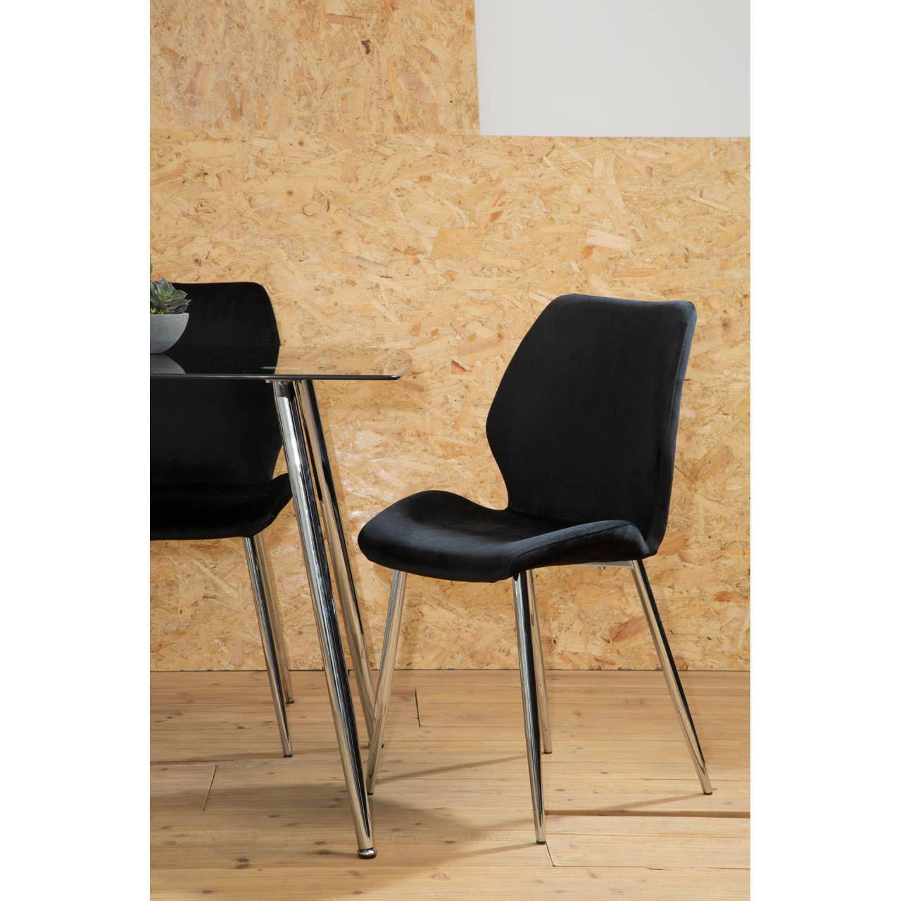 Black tempered glass dining table paired with six sleek black chairs featuring curved backs and chrome legs, set against a light wooden backdrop