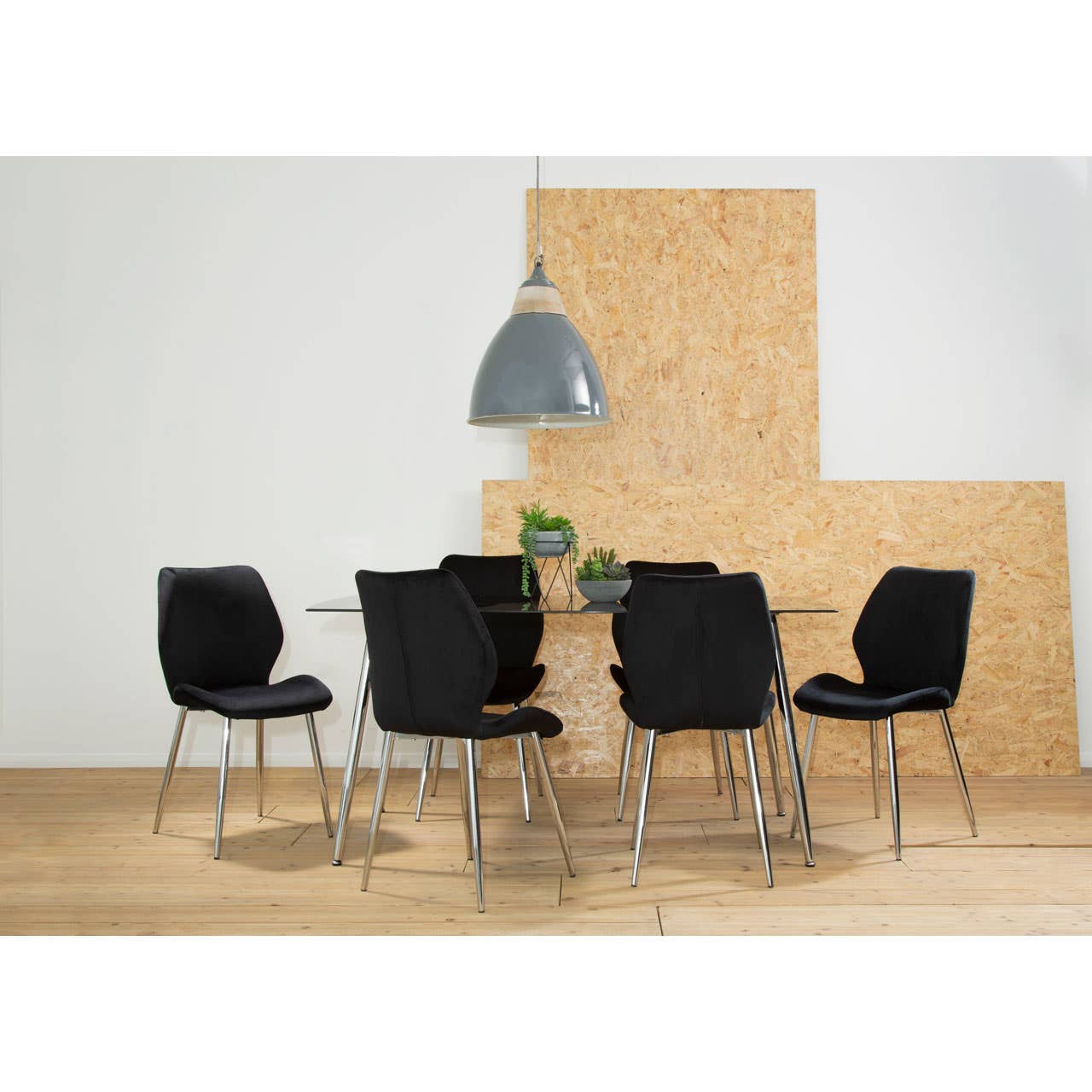 A sleek black tempered glass dining table surrounded by six modern black upholstered chairs with chrome legs, set against a light wooden floor and a textured beige wall. A stylish pendant light hangs above the table, adding a contemporary touch to the dining area