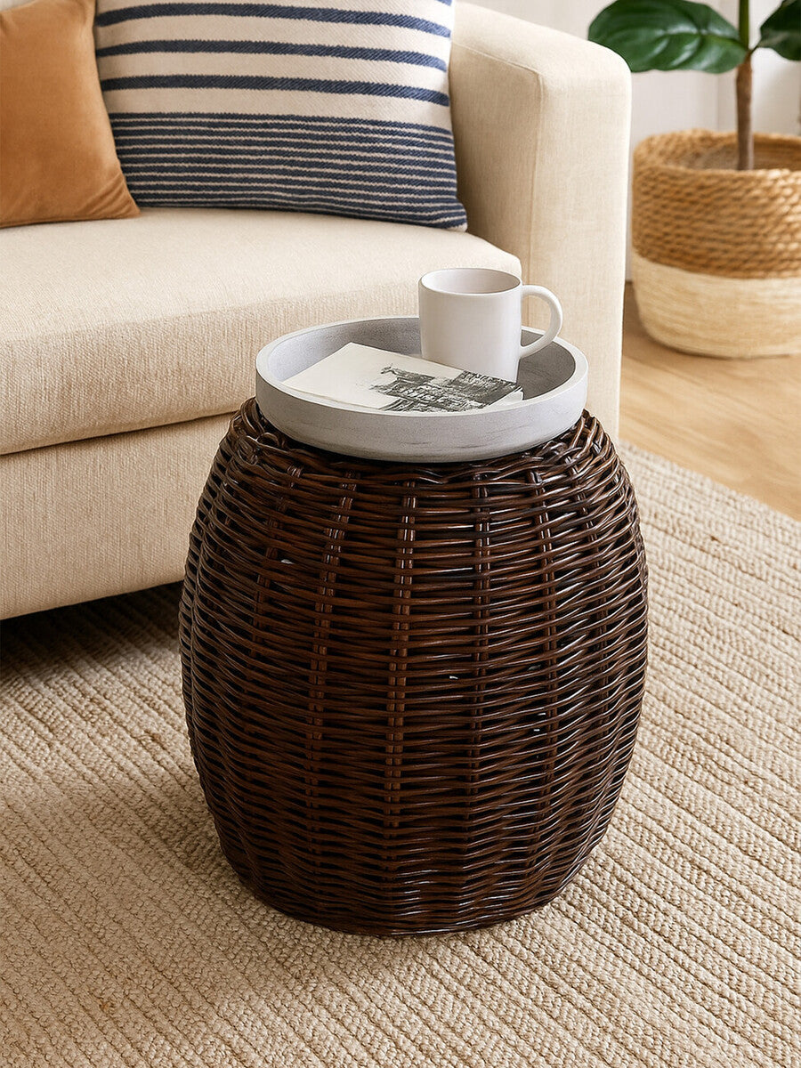A round, dark brown rattan stool with a textured, croco pattern and a light-colored marble top, placed next to a beige sofa on a woven rug. A white cup is resting on the marble surface