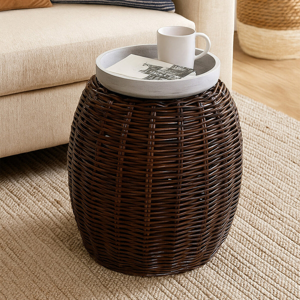 Natural croco rattan stool with a rounded, textured design in dark brown, featuring a flat, light-colored top that holds a white cup. The stool is placed on a light-colored woven rug, with a soft beige sofa visible in the background