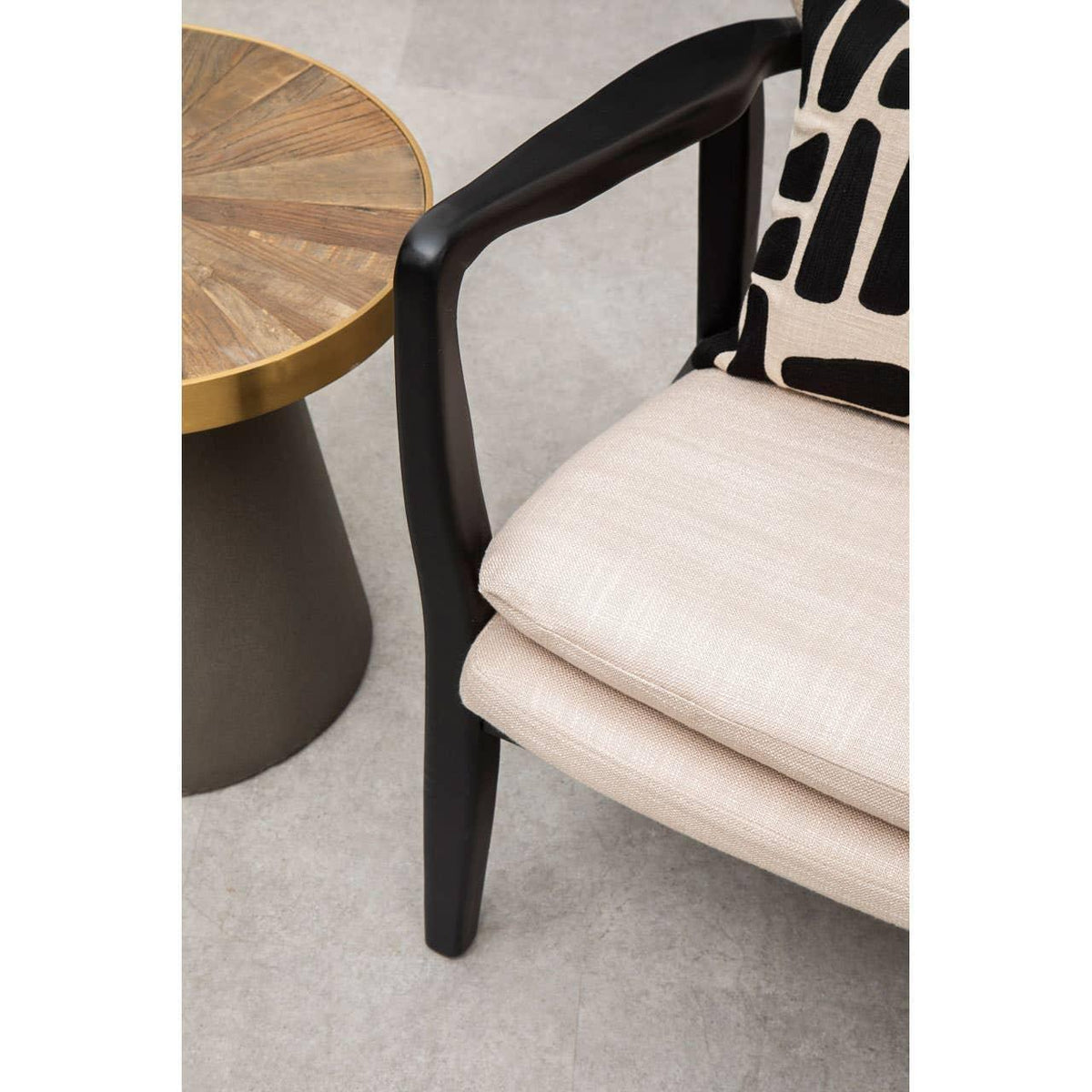 Modern accent chair with cream cushions beside round wood and brass side table