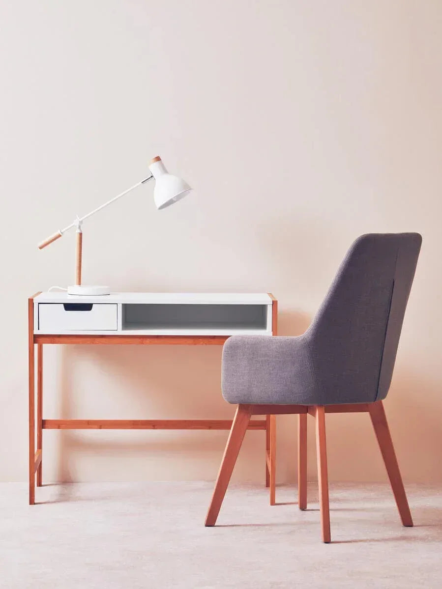 Wooden desk with white drawer, grey upholstered chair, and white desk lamp