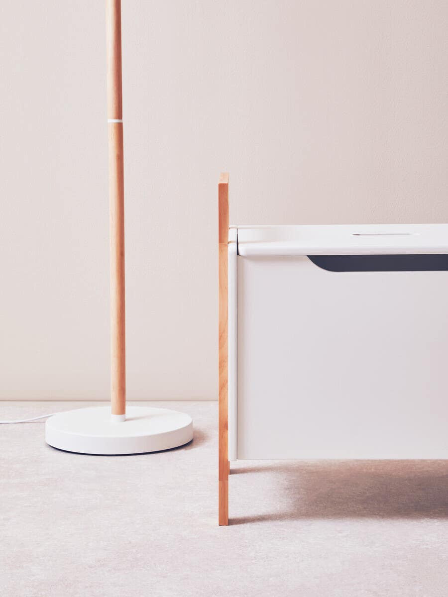 A white storage box with a sleek design featuring a single drawer, complemented by a minimalist floor lamp with a thin wooden pole and a round base. The background is a soft, neutral color, enhancing the modern aesthetic of the furniture