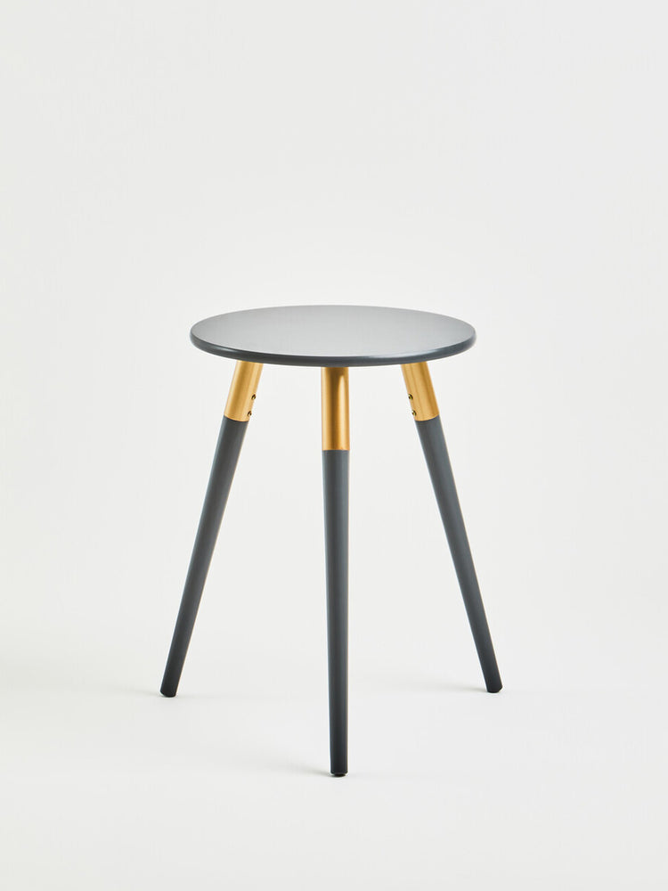 Dark grey side table with a round top and three tapered legs, featuring gold accents where the legs meet the tabletop. The design is modern and minimalist, suitable for various home decor styles. The background is plain and neutral, emphasizing the table's sleek appearance