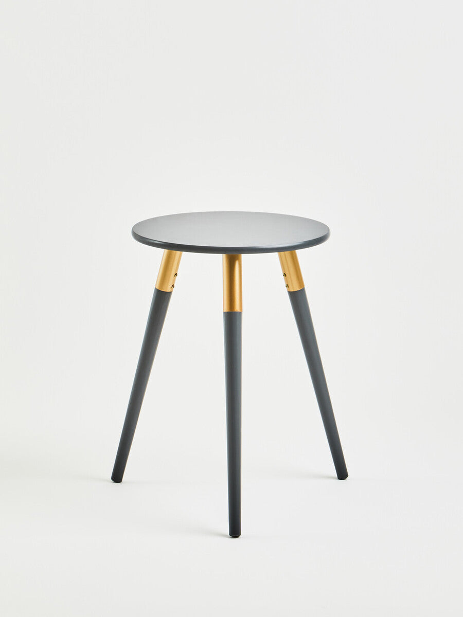 Dark grey side table with a round top and three tapered legs, featuring gold accents where the legs meet the tabletop. The design is modern and minimalist, suitable for various home decor styles. The background is plain and neutral, emphasizing the table's sleek appearance