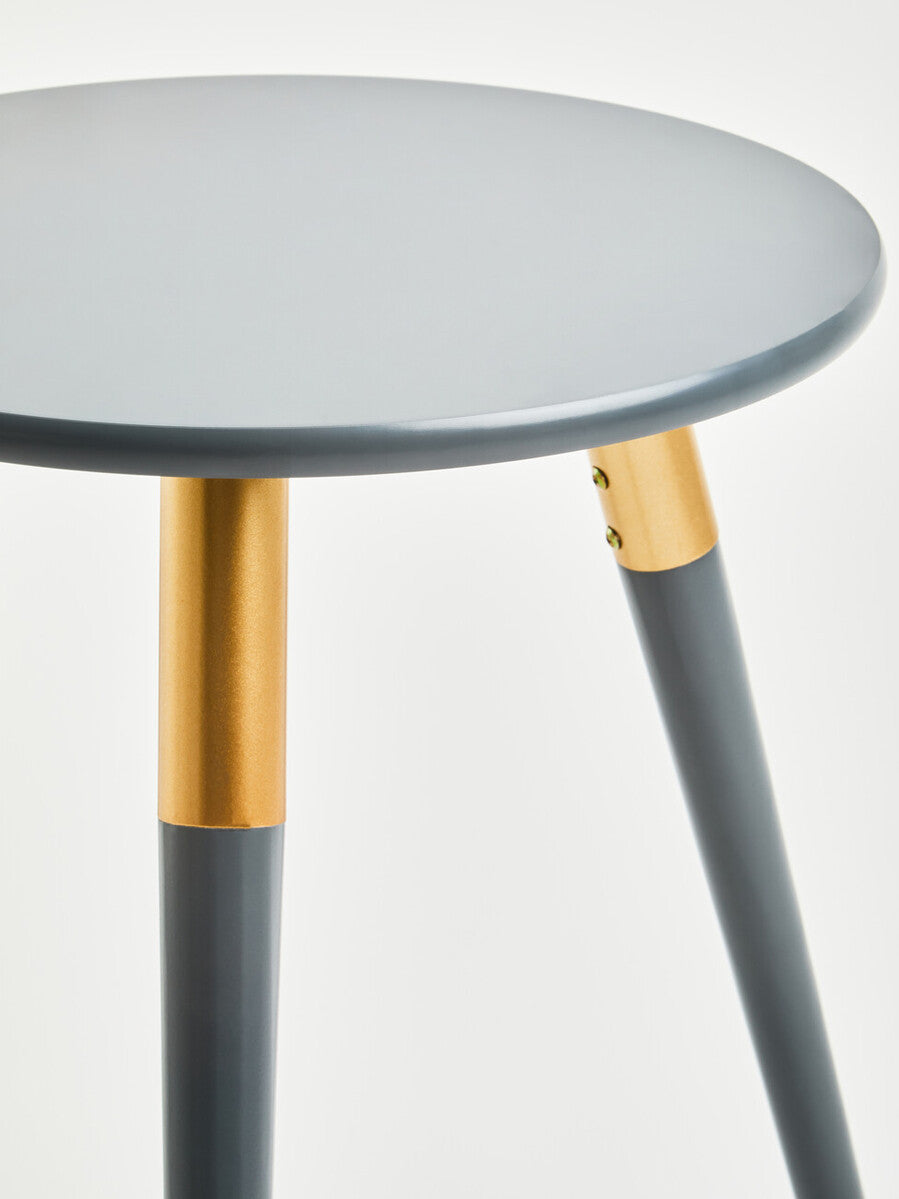 Round dark grey side table with a smooth surface and three tapered legs. The legs feature a contrasting light wood accent near the top, adding a modern touch to the design. The overall look is sleek and contemporary, suitable for various home decor styles