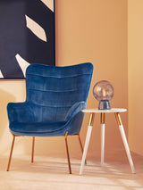 Light grey side table with tapered wooden legs, positioned next to a blue upholstered armchair. A decorative globe sits atop the table, against a warm, neutral wall background