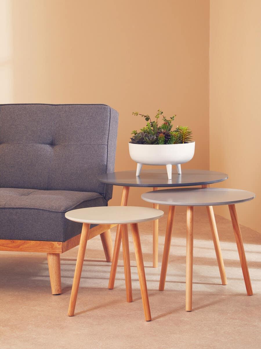 set of three round wooden side tables beside a grey fabric sofa, plant on top table