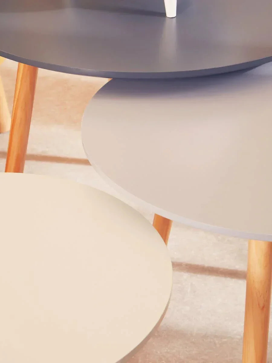 Set of three round nesting tables with wood legs in cream, grey, and dark grey finishes