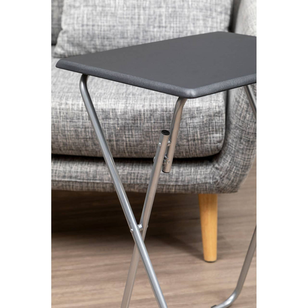 Folding table with a sand black top and silver metal legs, positioned next to a textured gray sofa, showcasing a modern and compact design suitable for small spaces