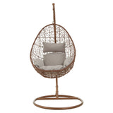 Brown rattan hanging chair with an egg-shaped design, featuring a cushioned seat in a light gray color and supported by a sturdy circular base. The chair is suspended from a vertical pole, creating a stylish and modern look suitable for indoor or outdoor use