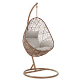 A brown rattan hanging chair with a unique teardrop shape, featuring a cushioned seat in a light gray fabric. The chair is suspended from a curved metal stand, which has a circular base for stability. The woven rattan design showcases an intricate pattern, adding a stylish touch to the overall look