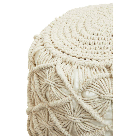 A close-up view of a round, knitted pouffe in a light beige color, featuring intricate woven patterns and a textured surface. The pouffe has a slightly rounded top and a sturdy, soft appearance, suitable for use as a footrest or additional seating