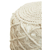 A close-up view of a round, knitted pouffe in a light beige color, featuring intricate woven patterns and a textured surface. The pouffe has a slightly rounded top and a sturdy, soft appearance, suitable for use as a footrest or additional seating