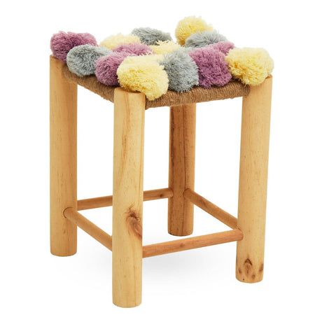 A wooden stool with four legs, featuring a top adorned with colorful pom poms in shades of grey, beige, pink, and yellow. The stool has a natural wood finish, highlighting its simple and modern design