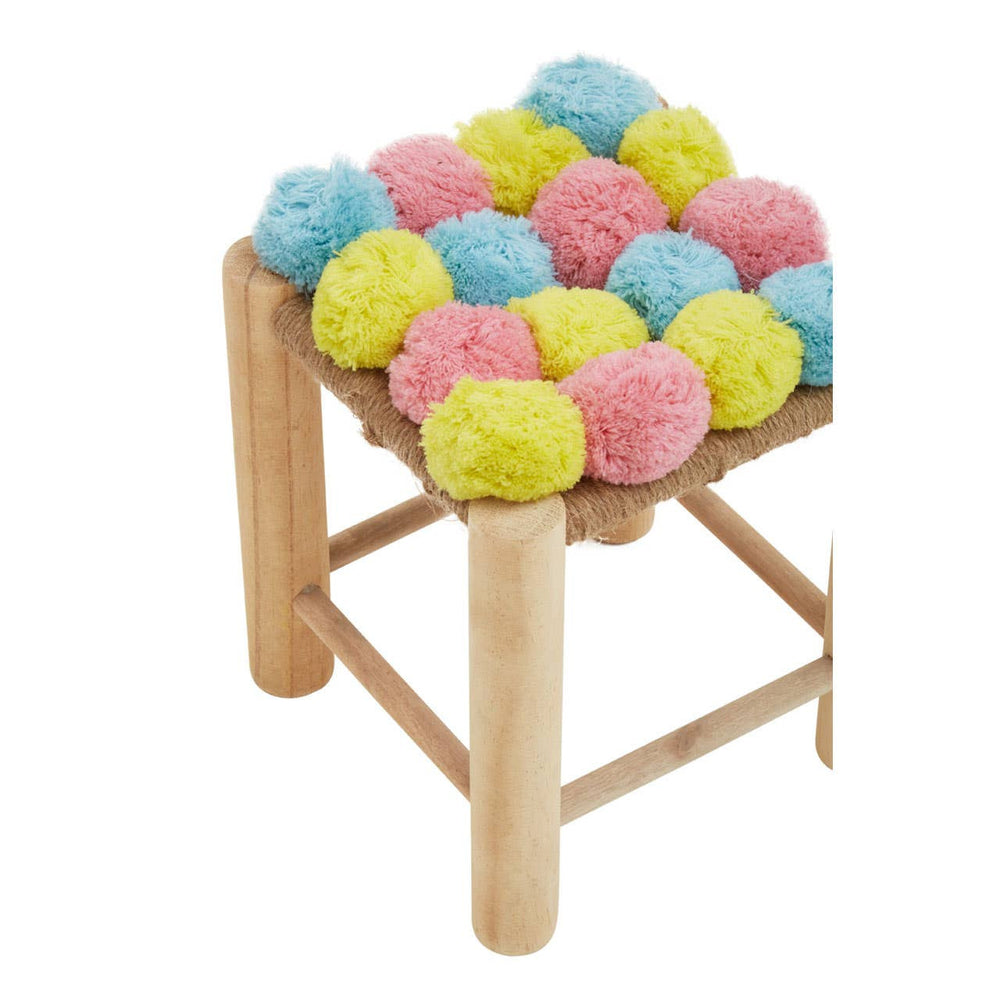A small stool featuring a colorful pom pom seat with pink, blue, and yellow pom poms arranged in a playful pattern, supported by light wooden legs