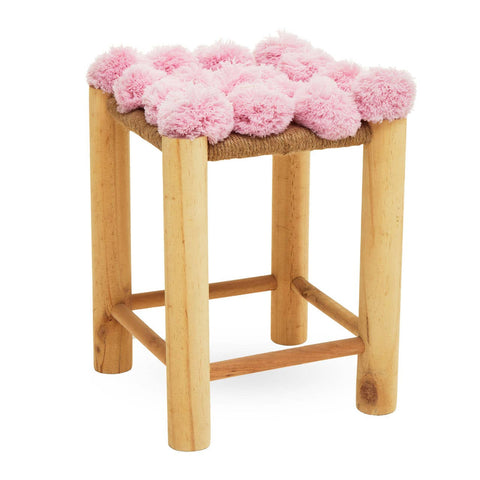 A wooden stool with light-colored legs and a top adorned with fluffy pink pom poms, creating a playful and whimsical design