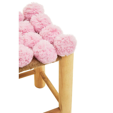 A close-up view of a stool featuring a soft, textured surface adorned with multiple pink pom poms, supported by light wooden legs