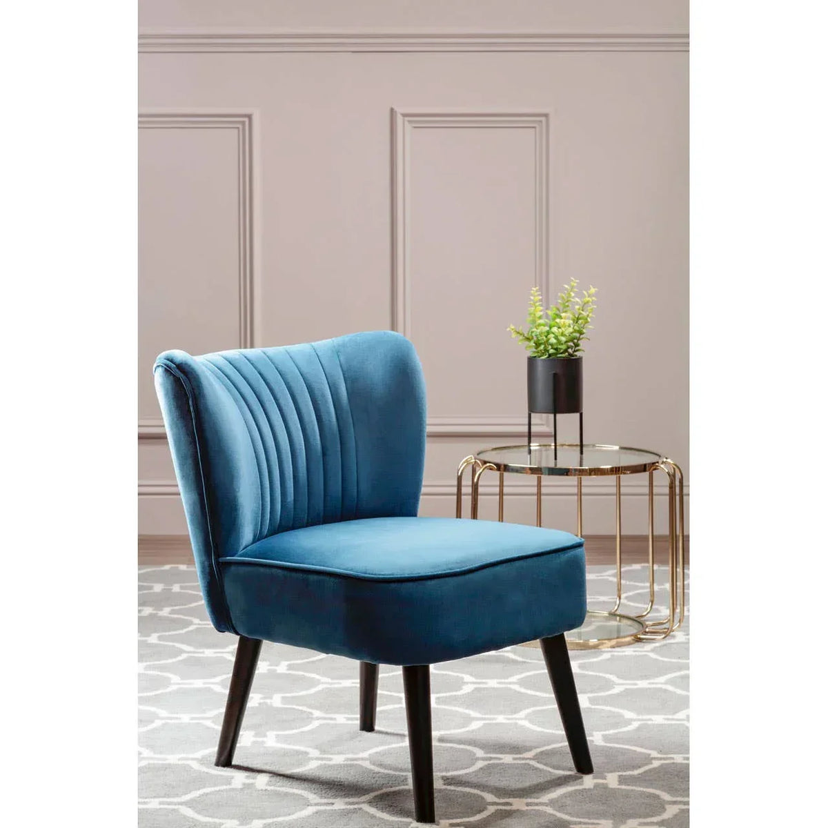Blue velvet accent chair with black legs beside gold metal side table and indoor plant
