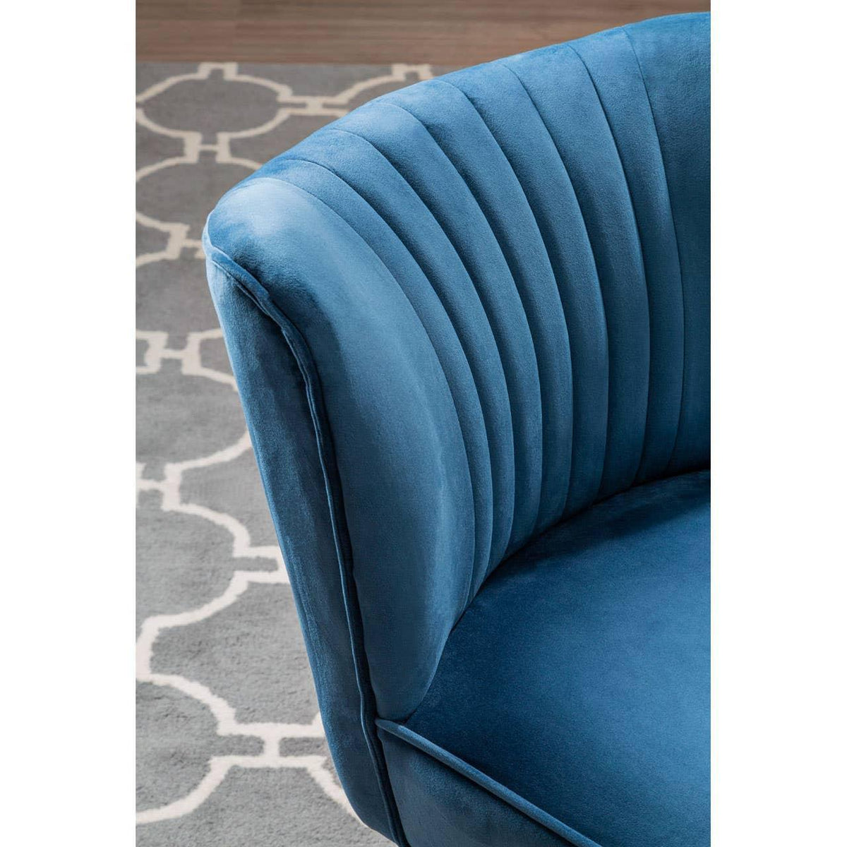 Blue velvet accent chair with vertical stitching detail on curved backrest, grey patterned rug