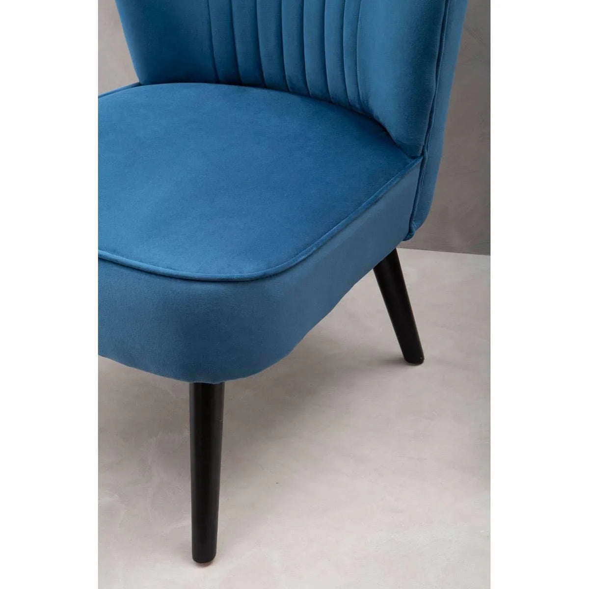 Blue velvet accent chair with vertical stitching and black wooden legs, side angle view