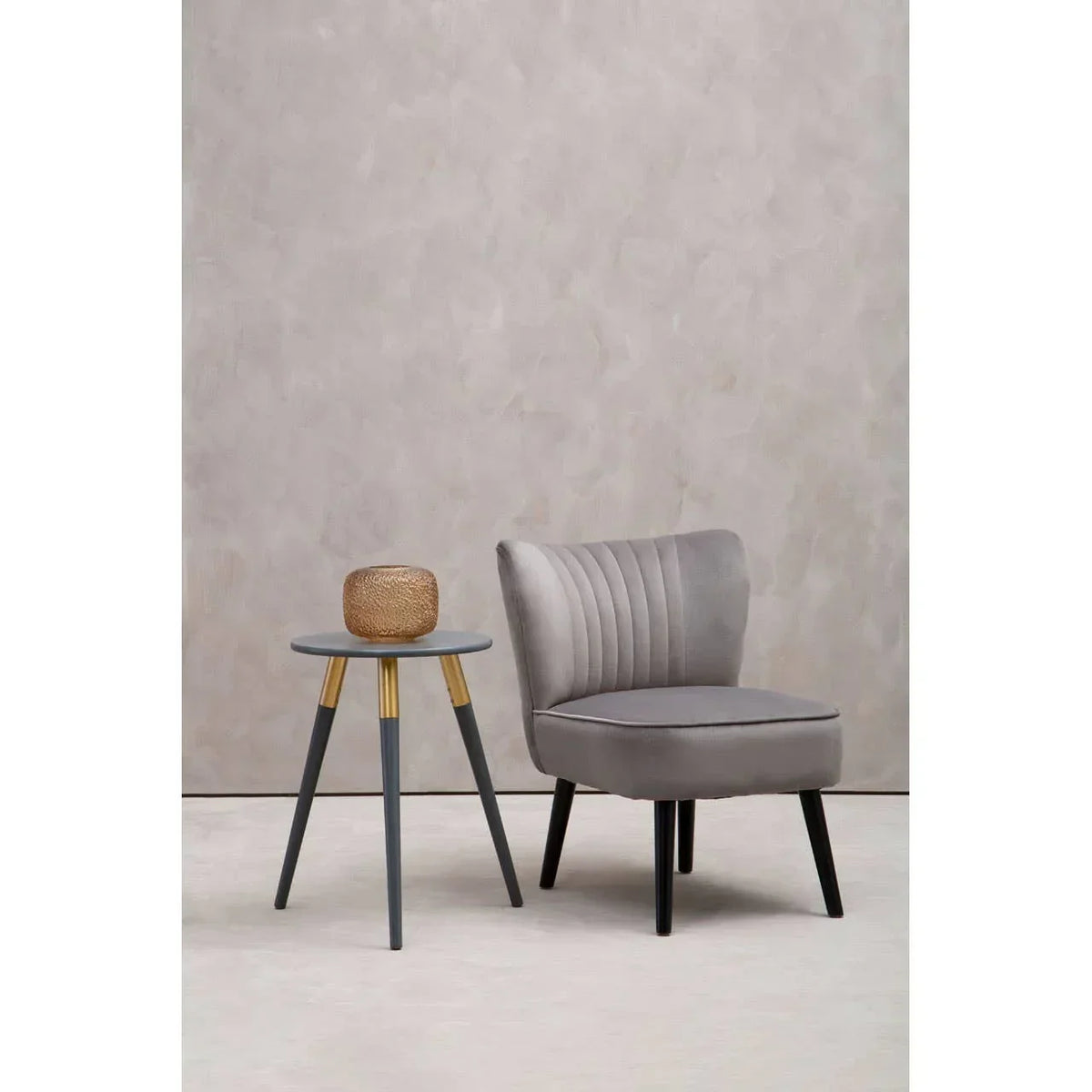 Grey velvet accent chair with fluted backrest beside round side table with gold accents