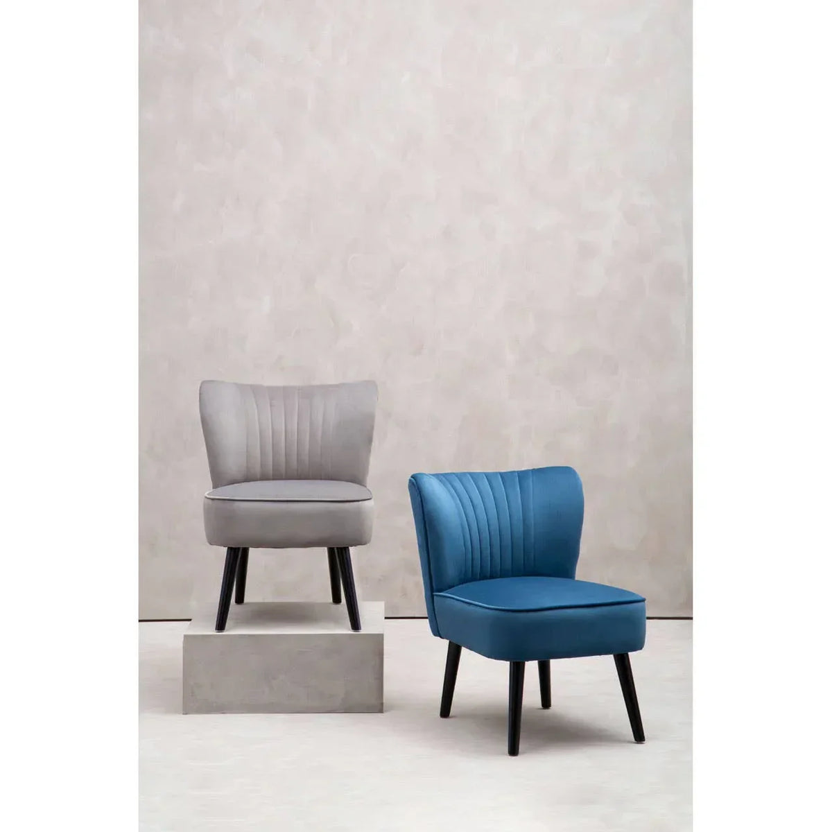 Grey accent chair and blue accent chair with black wooden legs against neutral backdrop