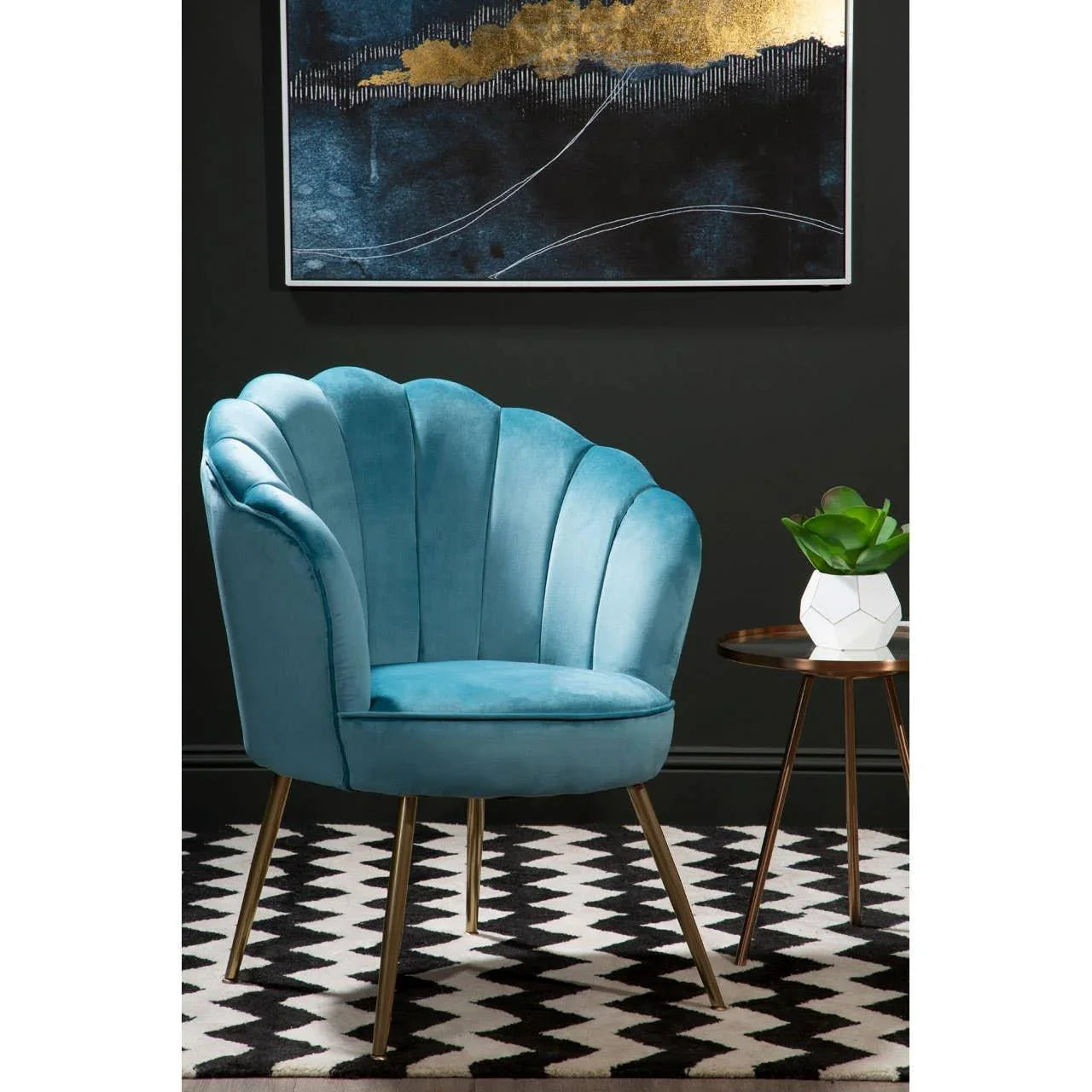 Blue velvet accent chair with gold legs beside round side table on patterned rug