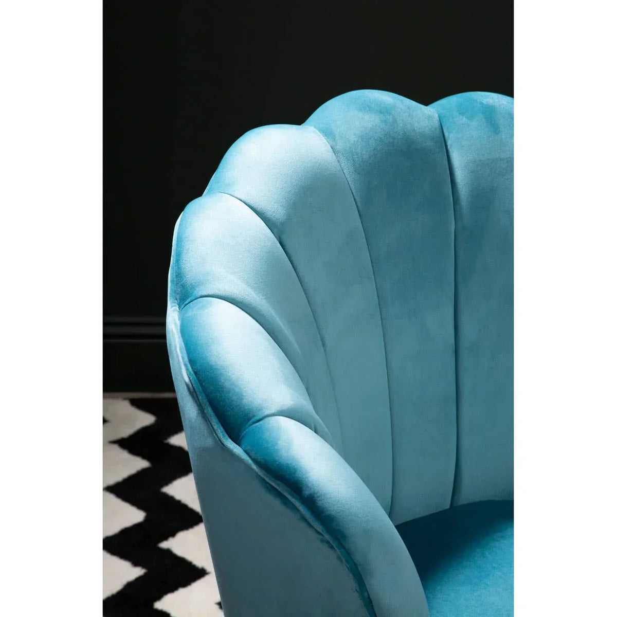 Close up of blue velvet accent chair with scalloped backrest on patterned rug