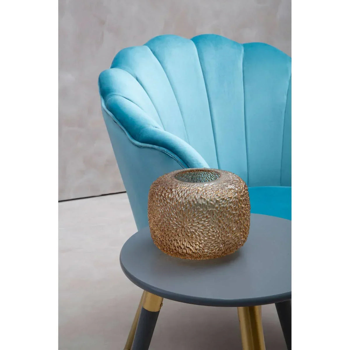 Blue velvet accent chair beside round side table with gold textured glass vase