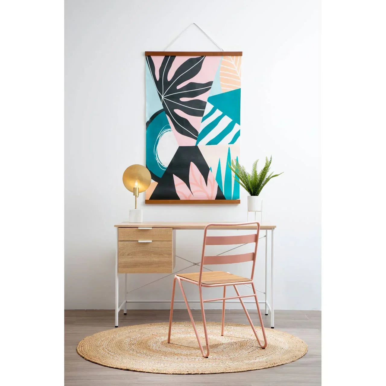 Modern home office desk with light wood drawers, pink chair, table lamp, and wall art
