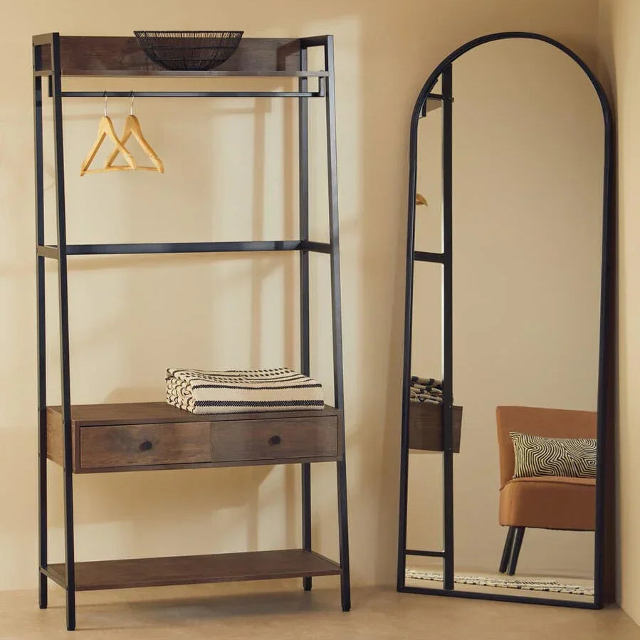 Industrial clothes rail with wooden shelves and drawers beside arched full length mirror