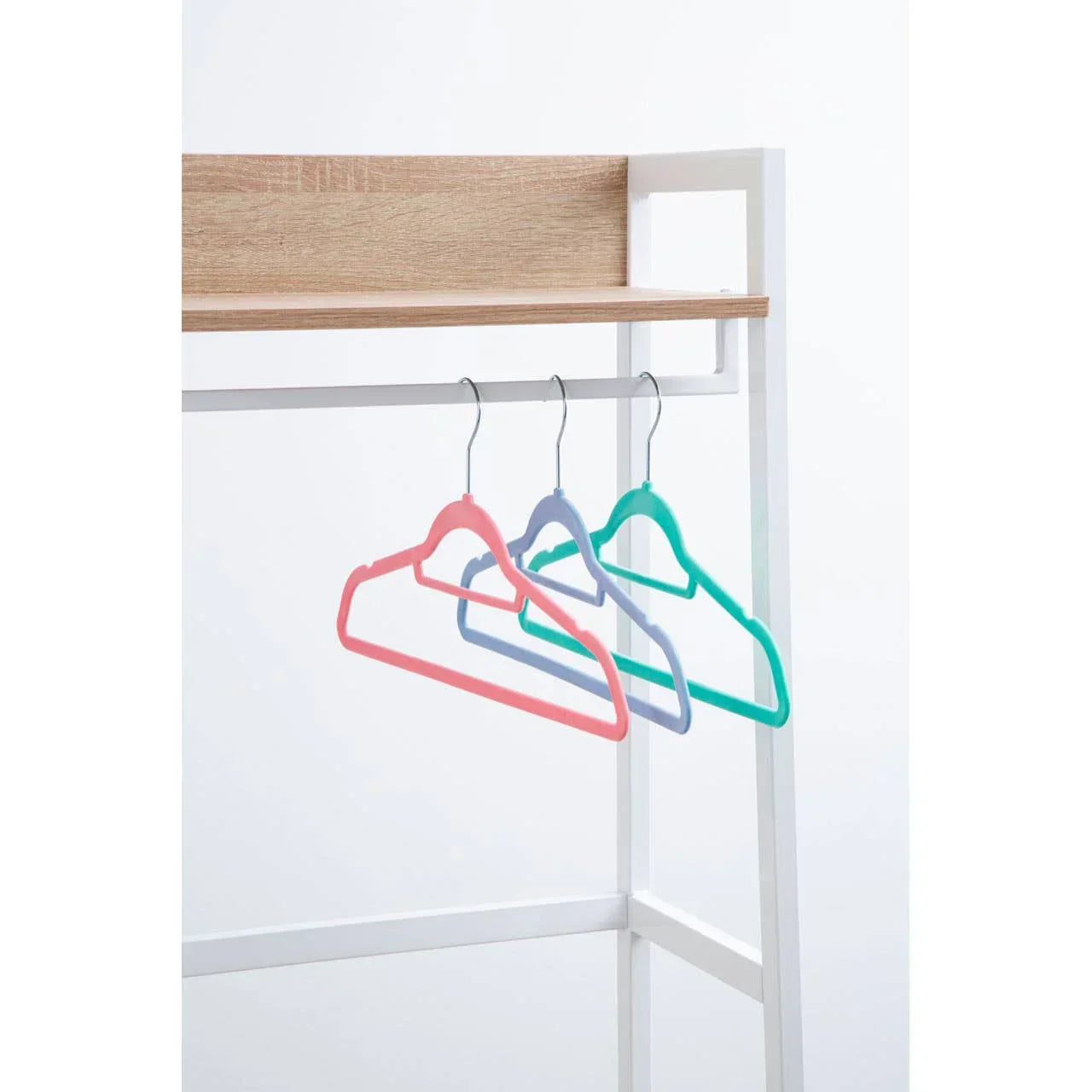 Multicolour plastic clothes hangers on white metal wardrobe rail with wooden shelf